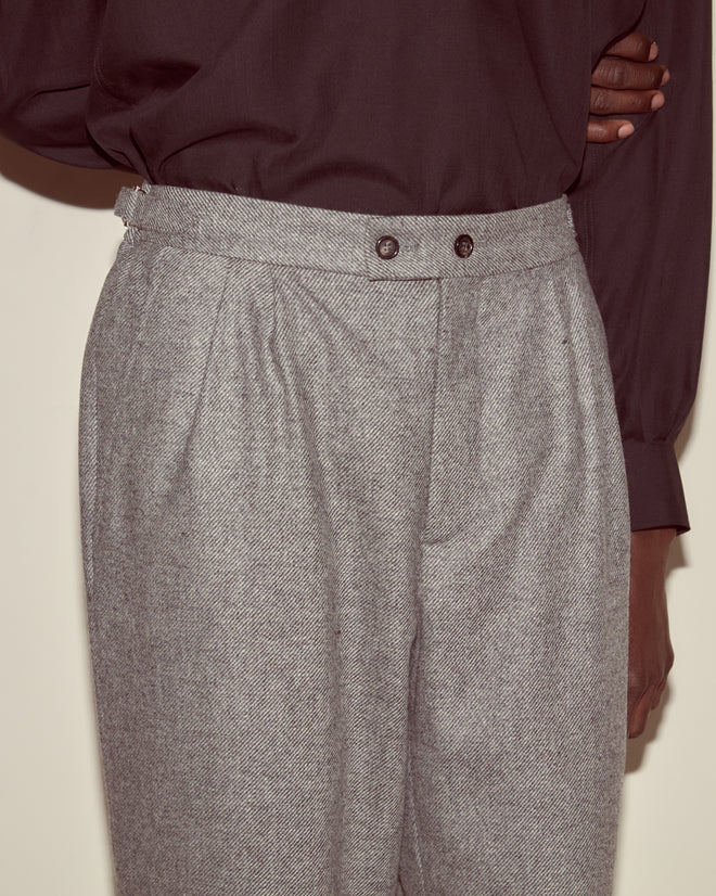Person wears Dovecote Trousers—high-waisted, grey trousers crafted from UK-woven wool—paired with a dark long-sleeved blouse, shown from the waist down for an elegant, modern suiting look.
