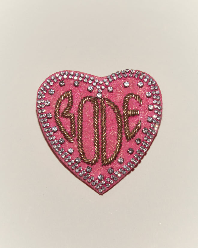 The Duchess Brooch features a pink heart shape with gold bullion embroidery spelling
