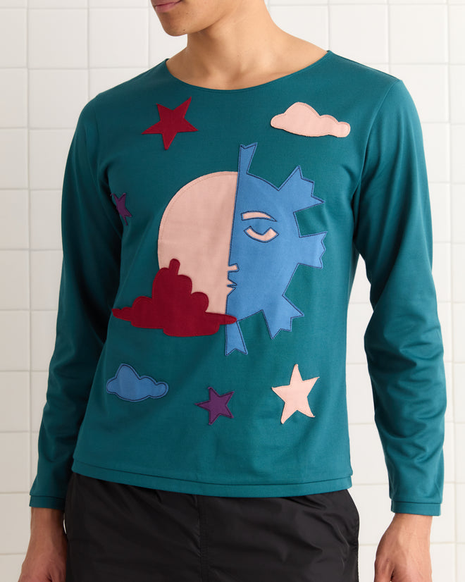 Person wearing the Eclipse Long Sleeve Shirt—a teal, vintage-inspired top with a front appliqué design featuring the moon, clouds, and stylized sun, moon, and stars.