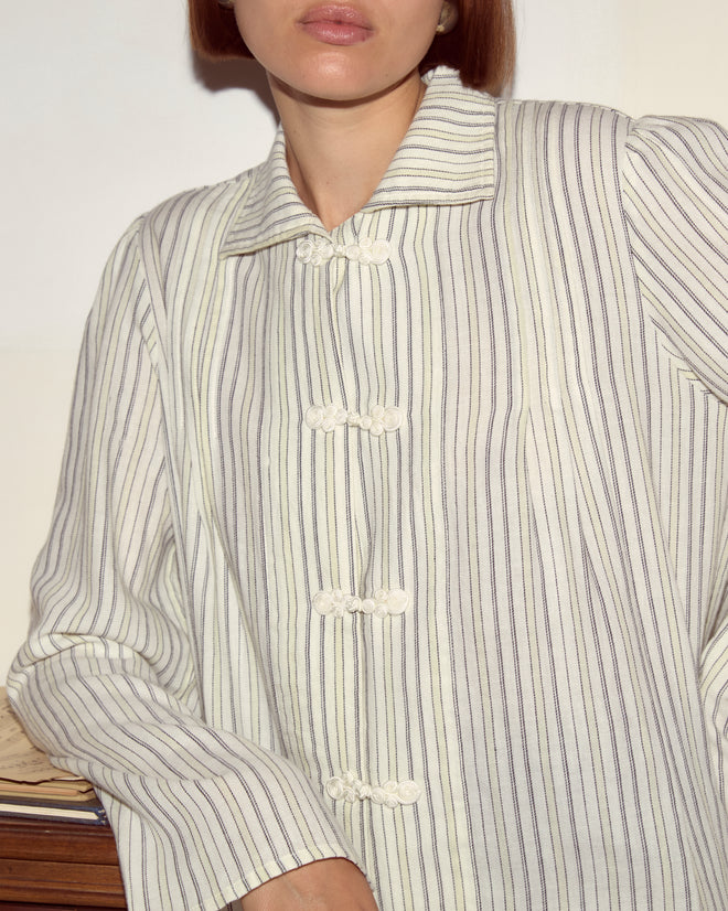 Woman in the Electric Light Blouse, a cream and black pinstripe button-up with pale yellow stripes, leaning against a surface, partially out of frame.