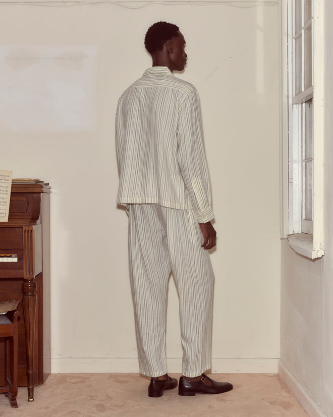 A person wearing the Electric Light Long Sleeve stands facing a wall near a window and a piano with sheet music.