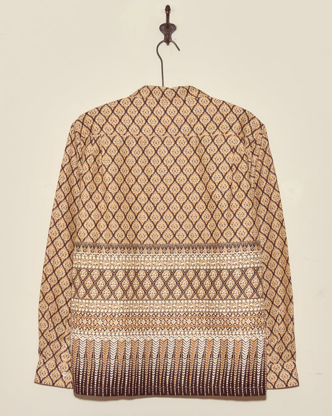 The Fictile Flame Long Sleeve Shirt - L/XL, featuring unique wax-print patterns, hangs on a hook against a simple, light-colored wall.