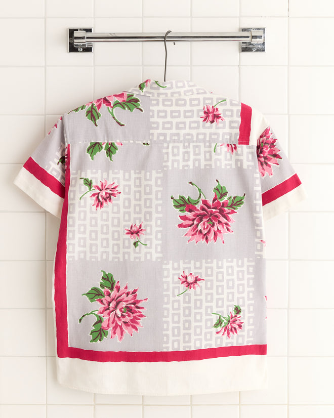 The Floral Kale Shirt - XS/S features short sleeves, a vintage pink floral and geometric print inspired by 1950s-1960s fashion, displayed against a tiled white wall.