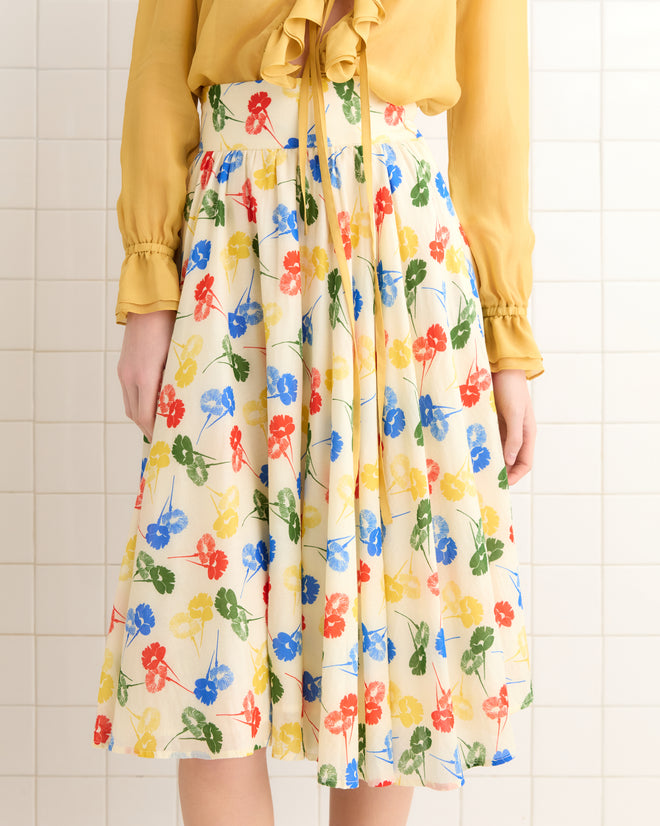 A person in a yellow blouse wears the Flower Stamp Skirt, made from 100% cotton with a vibrant floral pattern, while standing against a tiled wall.