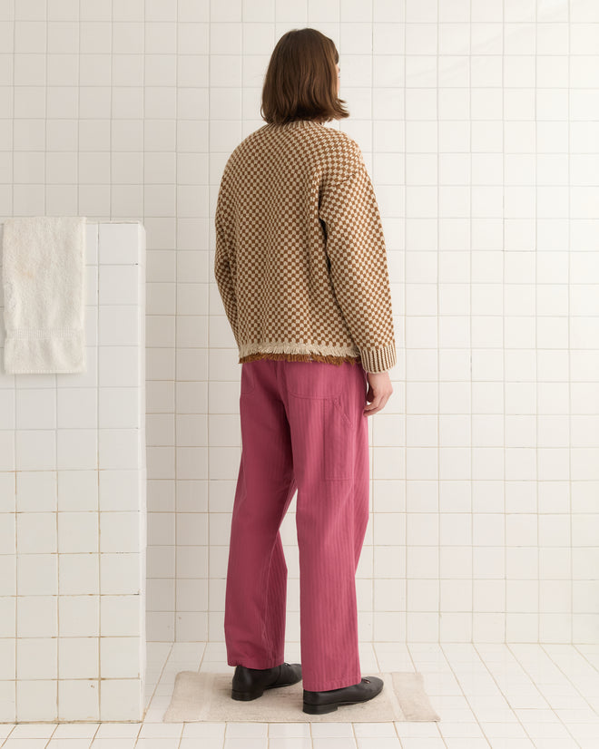 A person in a Fringe Check Pullover - Brown and pink pants stands in a tiled room, facing away.