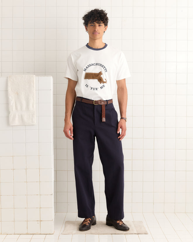 A man wearing the Fur Me Tee and dark pants stands in a white-tiled room, looking at the camera.