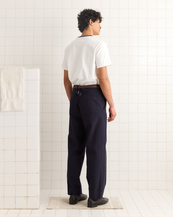 A man stands in a tiled room, facing away, wearing the Fur Me Tee, navy pants, and black shoes.