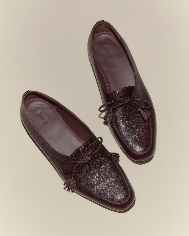 A pair of Tassel Shoes - Brown, crafted from vintage-style pebbled leather with elegant bows, displayed on a beige background.