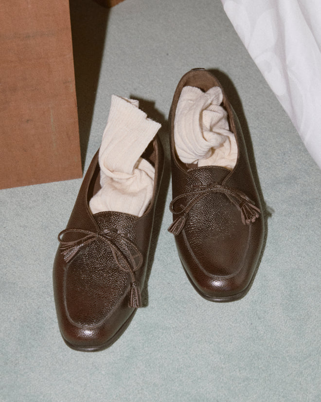 A pair of Tassel Shoes - Brown with cream socks tucked inside, placed on a light carpet.