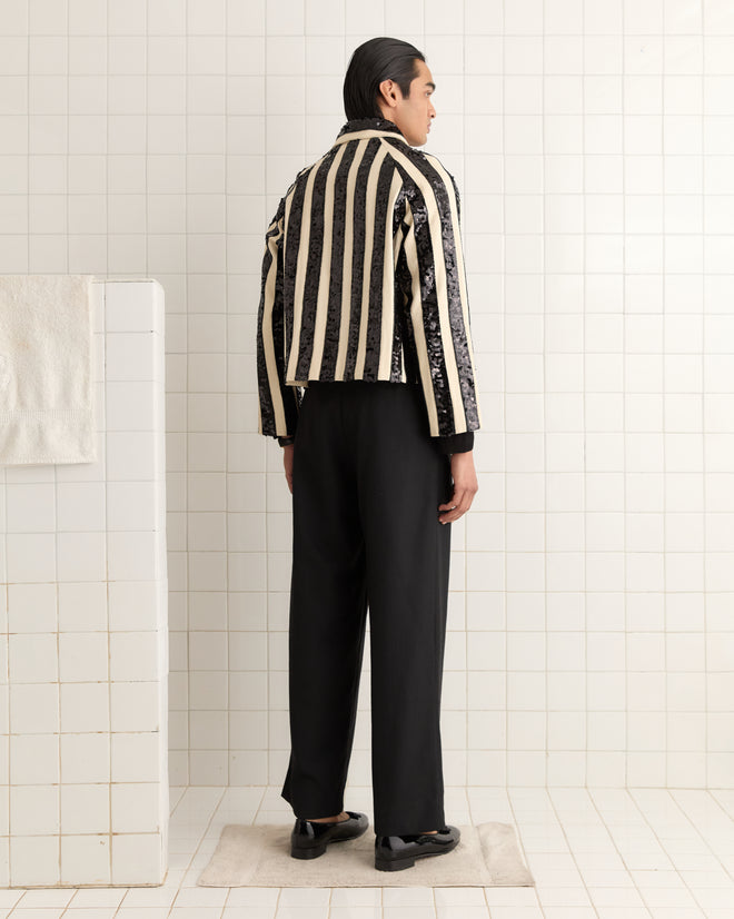 A man in a Grandstand Cropped Jacket with a boxy fit and striped design, along with black pants, stands facing away in a tiled room.