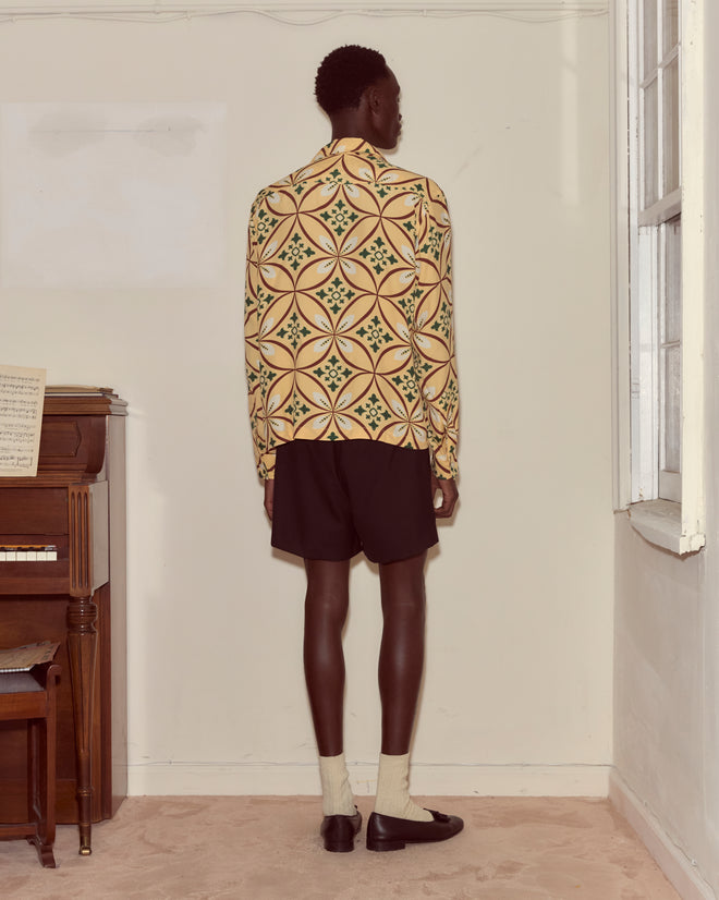 Person standing with back to camera wearing the Greer Long Sleeve Shirt, black shorts, socks, and black shoes in a room.