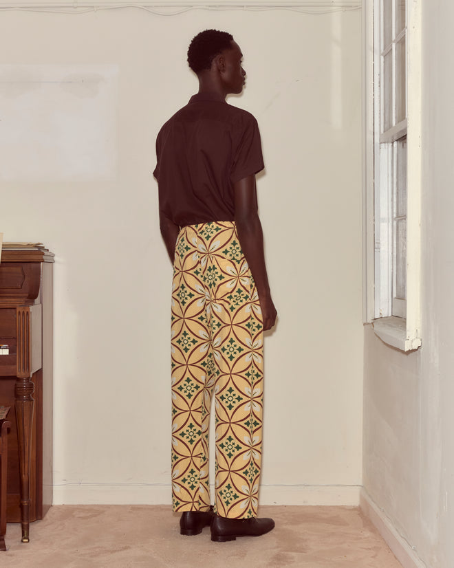 A person stands indoors facing a wall, wearing a black shirt and Greer Pajama Pants—wide-legged, viscose pants with a botanical print.
