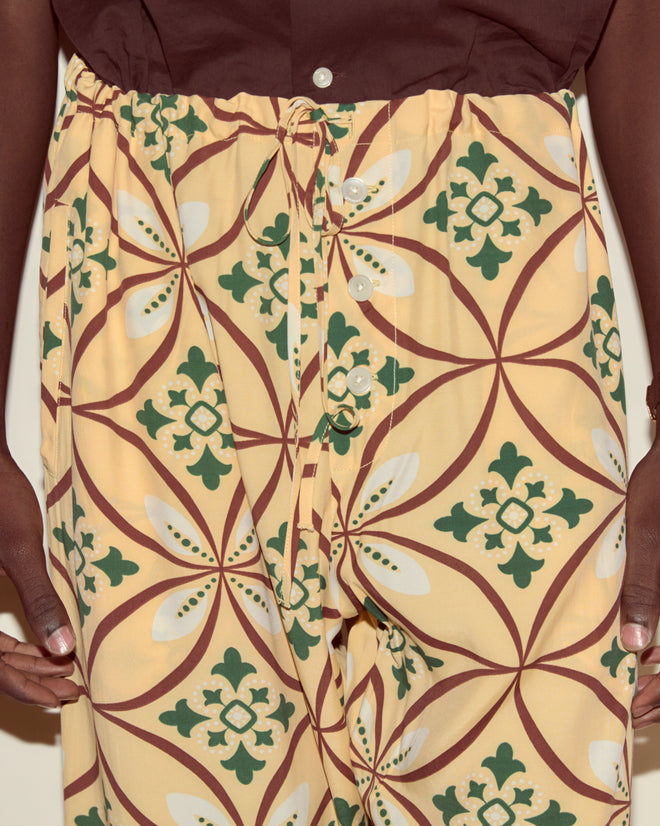A person wears Greer Pajama Pants, featuring a yellow base with a green and brown botanical print, holding the waistband with both hands.