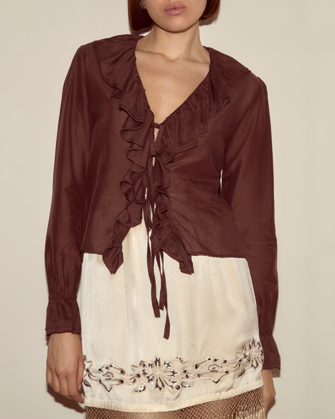 Woman wearing the Heartwood Flounce Blouse in deep burgundy cotton silk, paired with a cream skirt featuring embroidered floral details.