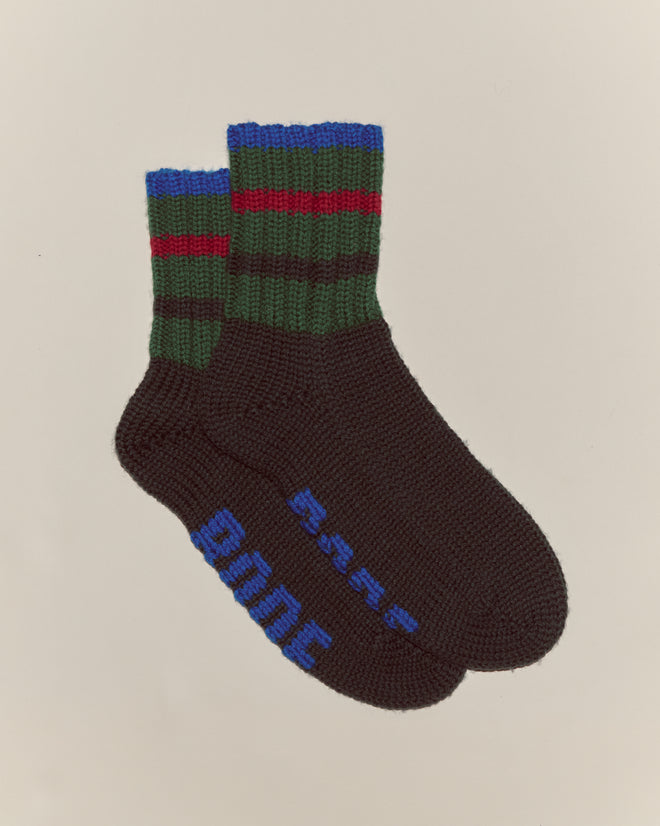 A pair of Herrington Stripe Socks - Green: chunky knit black socks featuring green and red stripes with blue text on the soles.