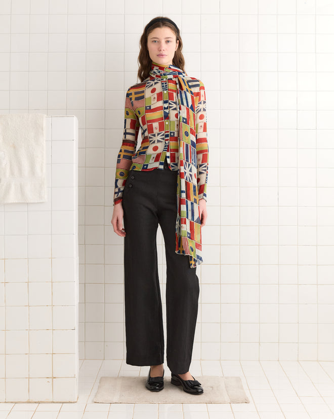 In a white-tiled room with a towel hanging on the wall, someone wears an International Blouse in vibrant silk paired with black pants.