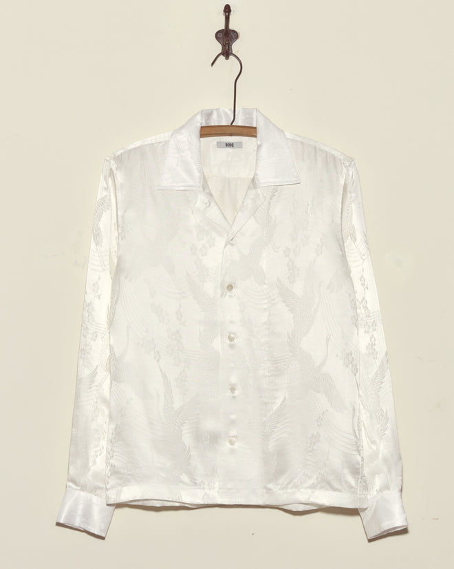 The Ivory Cloud Long Sleeve Shirt, crafted from deadstock jacquard with a subtle embossed pattern in white satin, is made in New York and displayed on a metal hook.