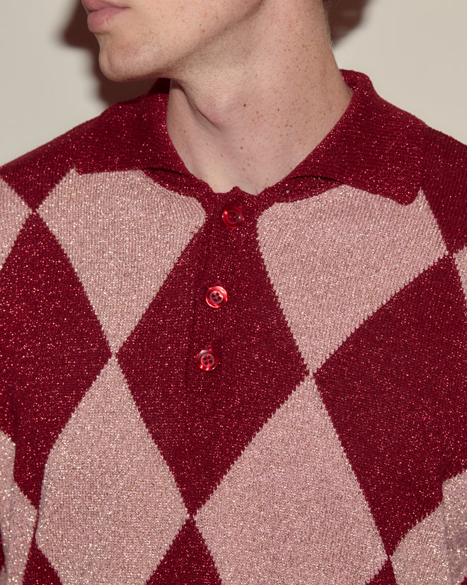 A person wearing the Jockey Polo, featuring a red and pink argyle knit pattern and three buttons, facing slightly to the left.