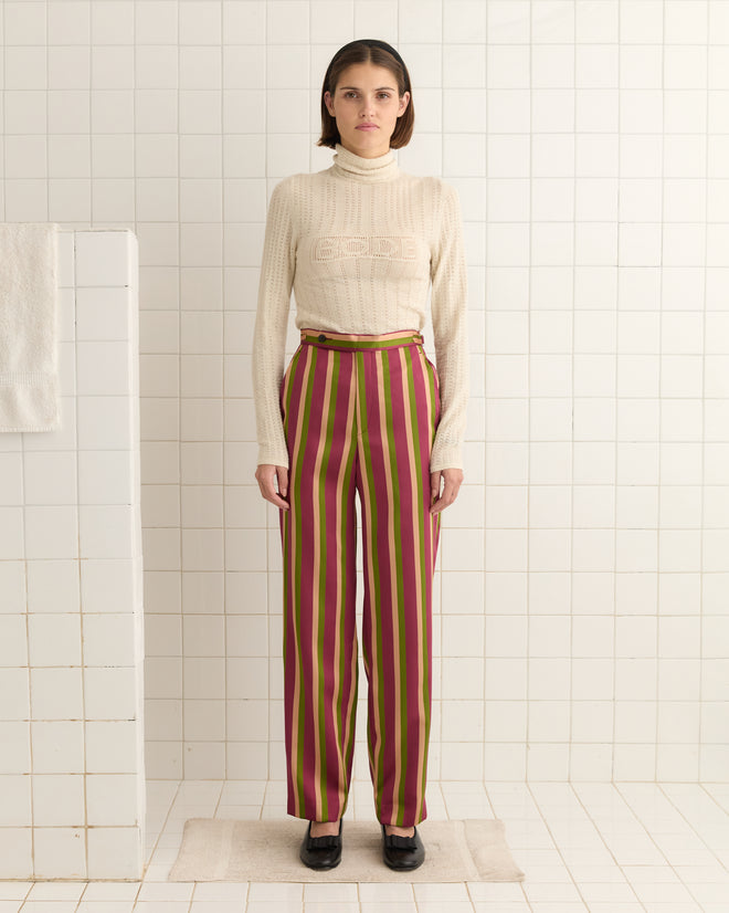 A person in Juniper Stripe Trousers, featuring luxurious Kutnu fabric, and a beige sweater stands on a tiled floor with a neutral expression.