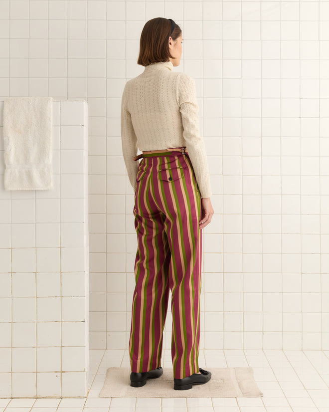 In a tiled room, a person in a cream sweater and Juniper Stripe Trousers with a side-tie waist stands facing away.