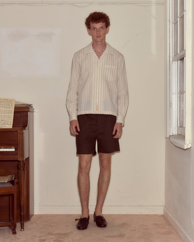 A young man stands indoors next to a piano and a window, wearing the Lavender Sail Shirt paired with dark shorts and loafers for a vintage-inspired look.