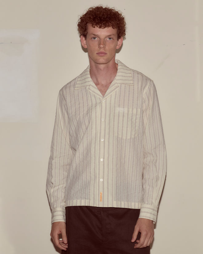 A man with curly hair wears the Lavender Sail Shirt and dark pants, standing against a plain wall.