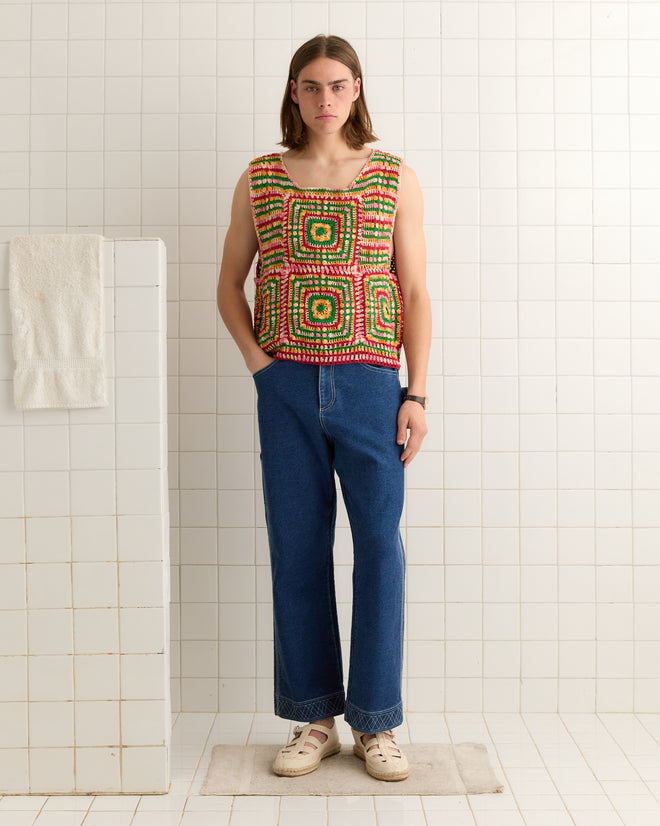 A person wearing a Manchester Crochet Tank and 100% cotton jeans stands in a tiled room, hands in pockets, facing forward.
