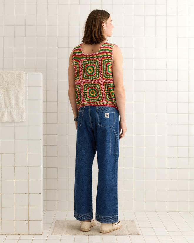Wearing a hand-crocheted Manchester Crochet Tank in vibrant hues and blue jeans, a person stands in a tiled room facing away.