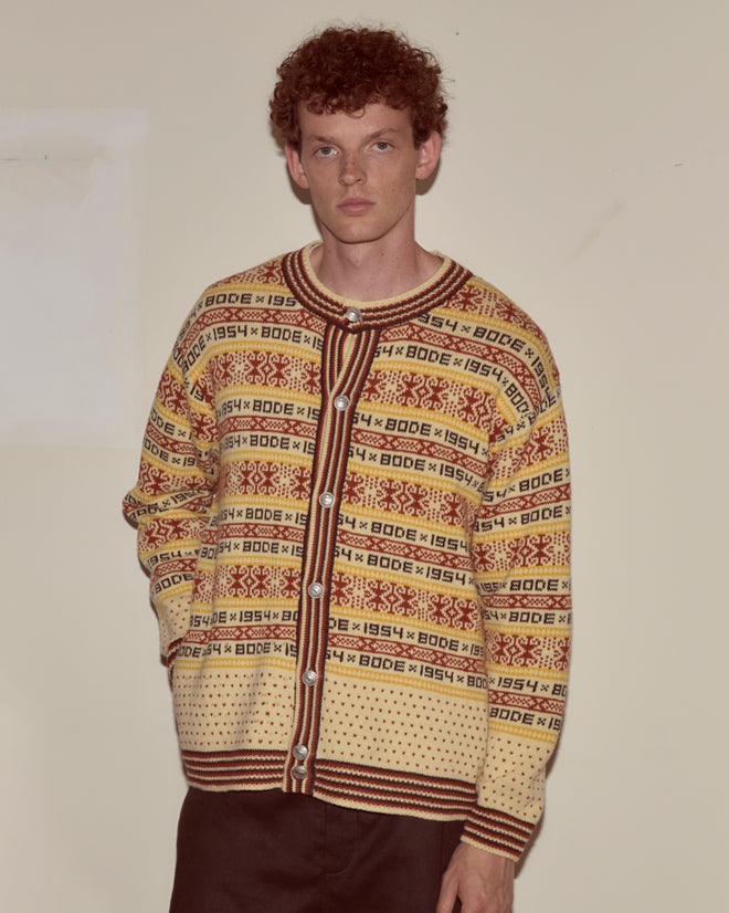 A man with curly hair wears the Marzipan Cardigan featuring a Norwegian pattern,
