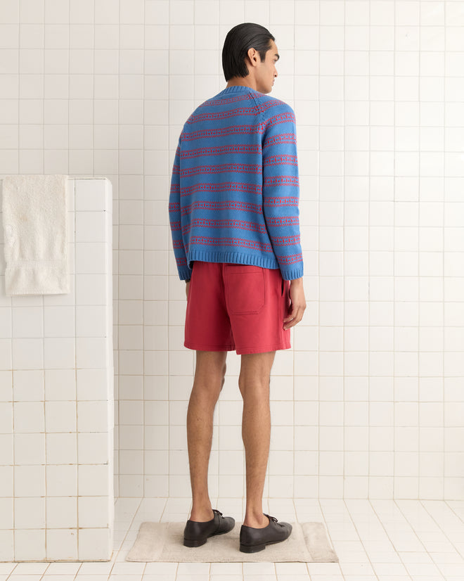 A person wearing the Meandering Stripe Cardigan in blue and red shorts stands in a tiled room, facing away.