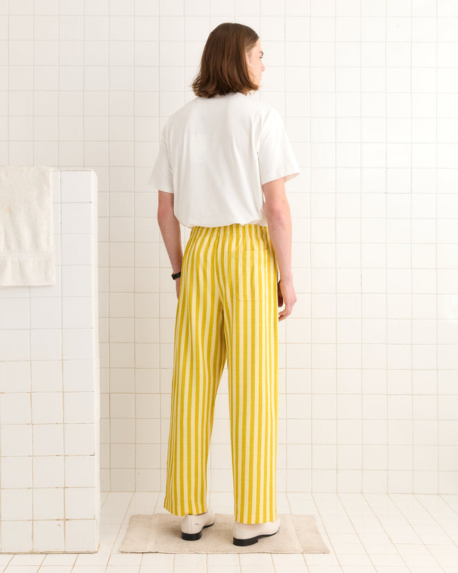 A person wearing a white shirt and Medalist Sweatpants - Yellow stands in a tiled room, facing away.