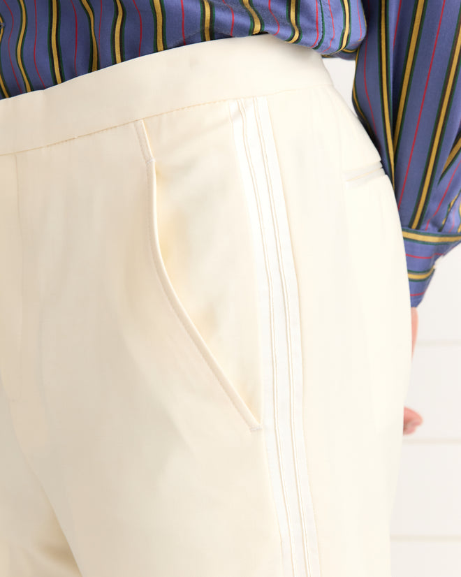 Close-up of a person wearing Meringue Smoking Trousers in ivory wool and a blue shirt with multicolored vertical stripes.