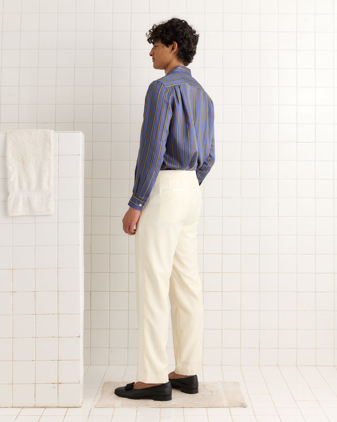 A person in a striped shirt and Meringue Smoking Trousers stands on a rug in a tiled bathroom, facing sideways.