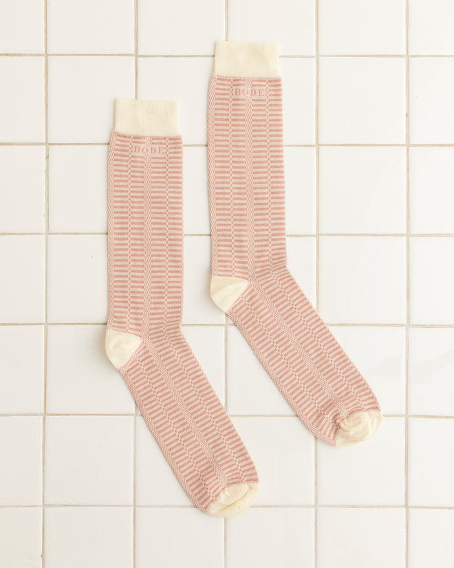 A pair of Micro Check Socks in pink and cream, featuring a retro pattern and cream toes, heels, and cuffs, rest on a white tiled surface.