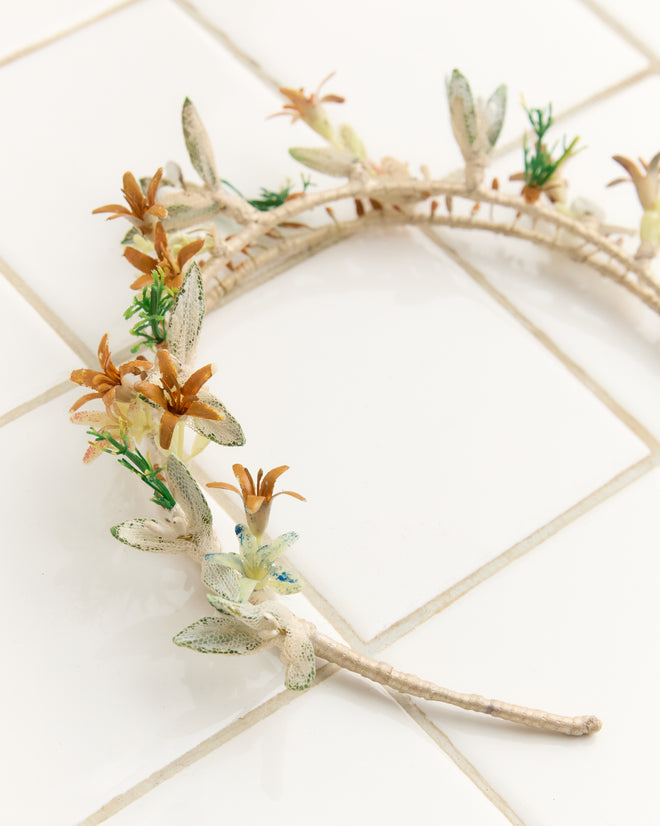 The Starflower Crown, adorned with small artificial flowers and leaves, rests on a white tiled surface—an elegant choice for anyone seeking vintage wedding accessories.