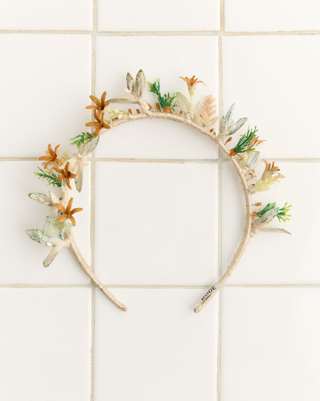The Starflower Crown is a vibrant headband adorned with artificial leaves and flowers—ideal for vintage wedding looks or standout floral crowns, beautifully showcased on white tile.