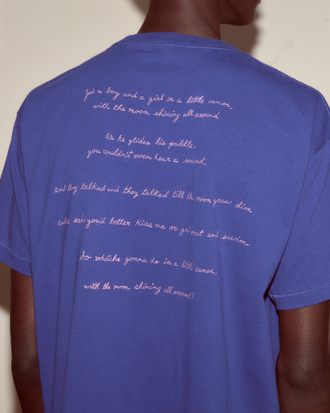 Person wearing the Moon Tee, a blue cotton t-shirt featuring handwritten white campfire song lyrics printed on the back.