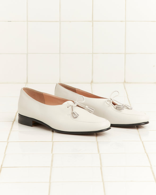 Tassel Shoes - White: Vintage white leather loafers with tassels, showcased on a white tiled floor and wall.