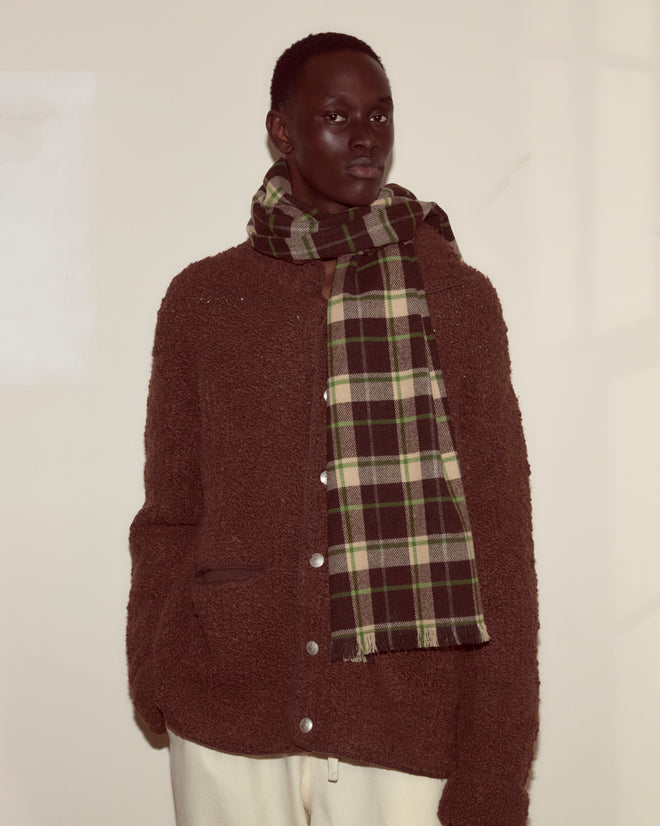 Person wearing a brown textured jacket, cream pants, and the Woodcrest Scarf from Camp Onibar, standing against a light wall.