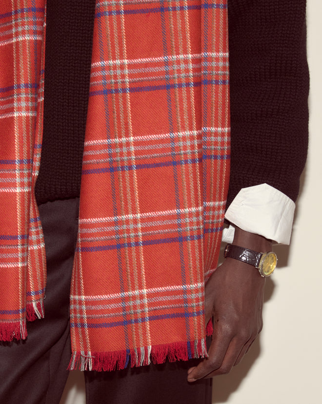 A person wearing the Gable Plaid Scarf in red wool, a black sweater, a white shirt cuff, and a black watch with a gold face.