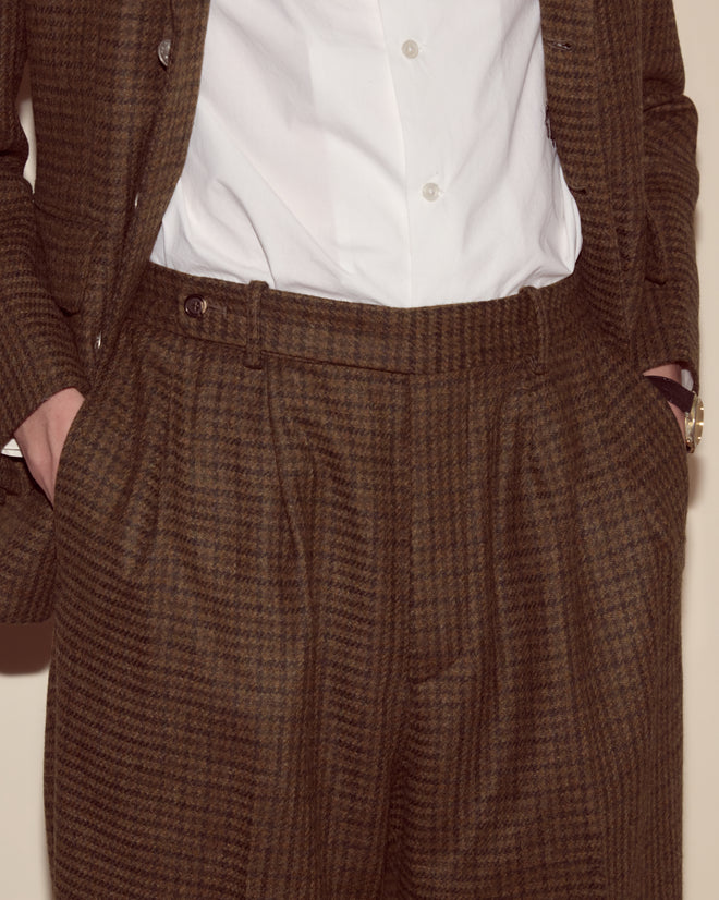 Person wearing Morris Houndstooth Trousers with a brown plaid suit, wide-leg silhouette, hands in pockets, and a white button-up shirt.