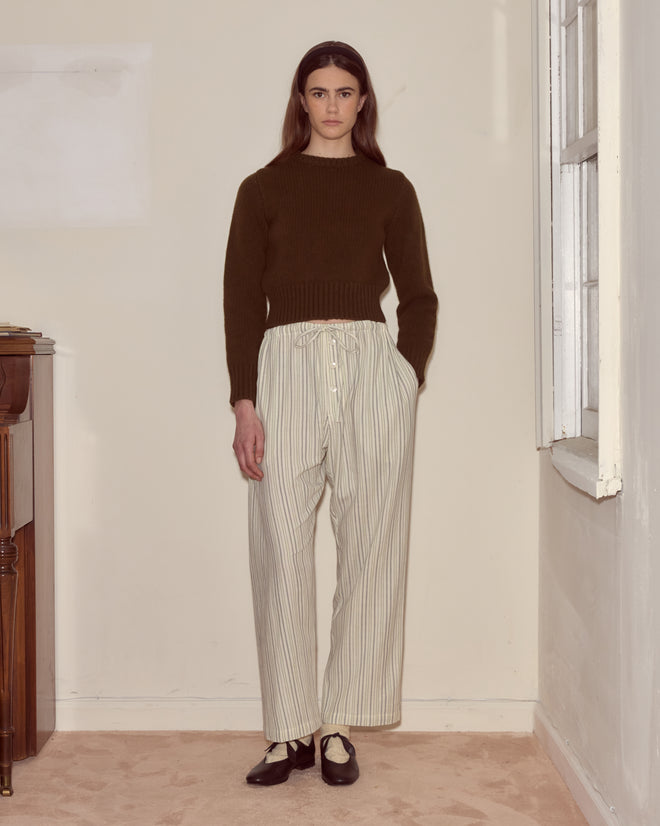 A person stands indoors by a window and piano, wearing a dark sweater paired with Electric Light Pajama Pants.