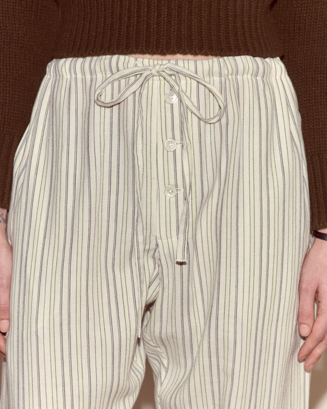 Close-up of a person wearing Electric Light Pajama Pants—cream with thin vertical stripes—paired with a cozy brown sweater.