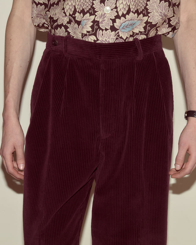 Person wearing Corduroy McNab Trousers in dark purple and a floral shirt, with hands relaxed by their sides.