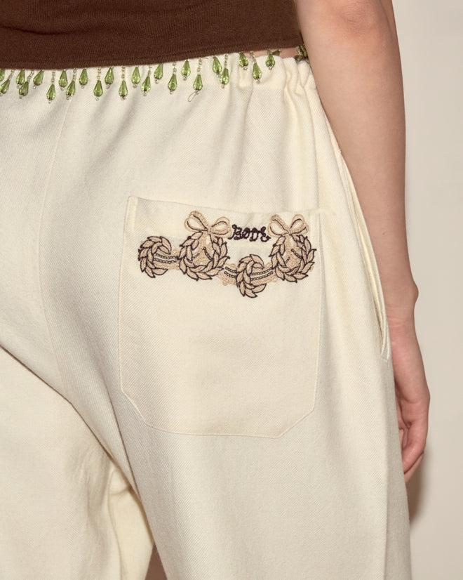 Close-up of Laurelist Pajama Pants in cream soft flannel with pocket embroidery and a leafy green garland trim on the waistband.