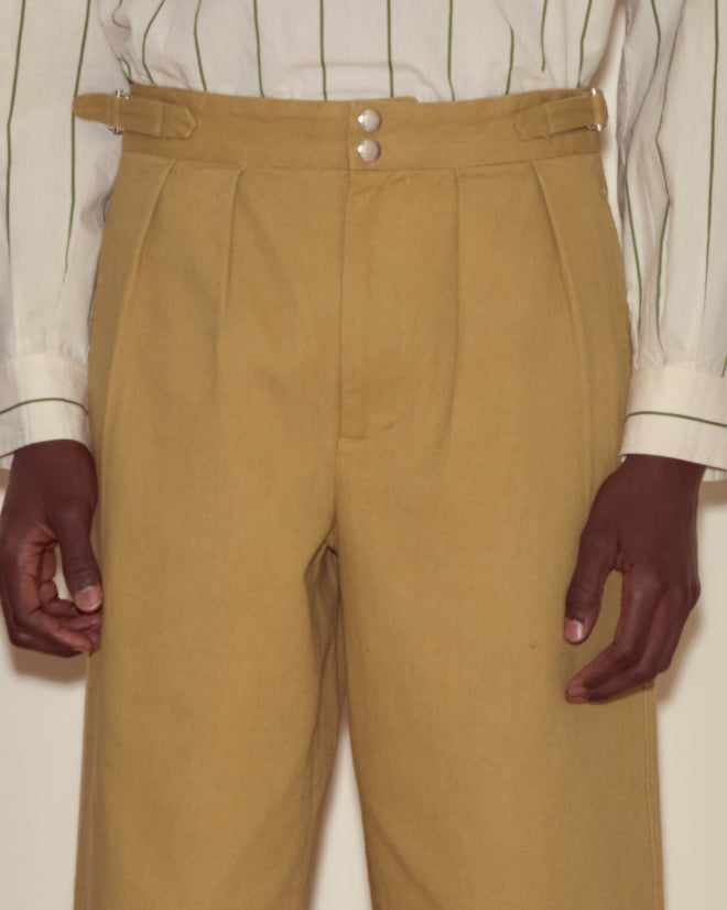 Person wearing Wide Leg Snap Trousers in khaki, inspired by vintage Australian military pants, paired with a white shirt featuring green stripes, hands at sides.