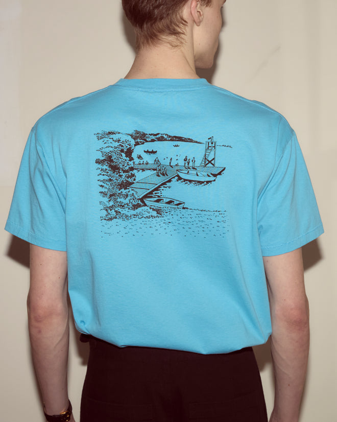 Person wearing a blue Laketown Tee featuring a black sketch of a lakeside scene with boats and people on the back, capturing the spirit of the Poconos.