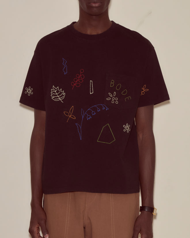 Wearing the Embroidered Field Guide Tee, made from black 100% cotton and featuring colorful embroidered leaves, flowers, and