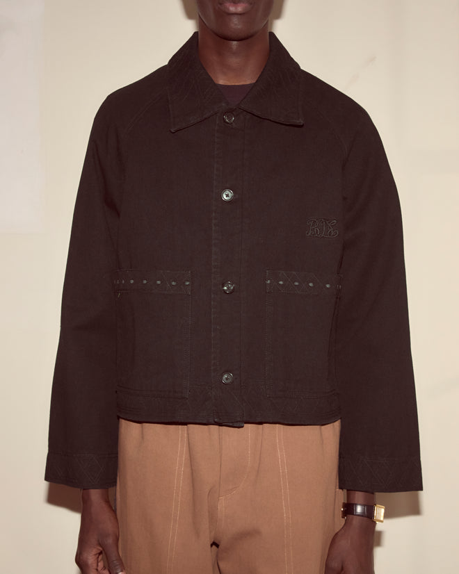 A person wearing an Embroidered Denim Jacket - Black and tan pants, standing against a plain light background.
