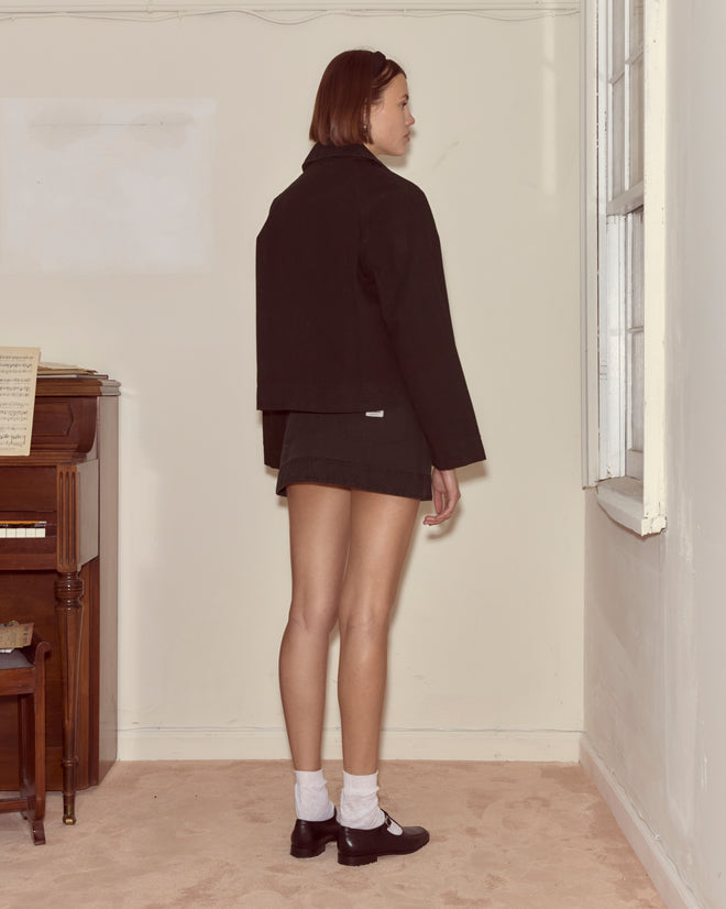 A woman wearing the Embroidered Denim Jacket - Black, featuring a boxy fit, stands indoors by a window with her back to the camera.